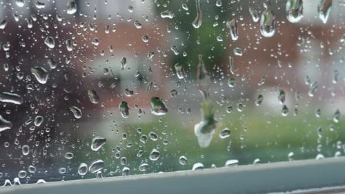 Raindrops fall and flow down the window glass. Close up. Blurred background.