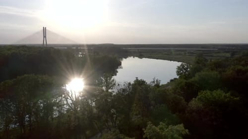 Luftaufnahme eines breiten, ruhigen Flusses mit einer großen Kabelbrücke, die in der Ferne sichtbar ist. Sonnenreflexion o