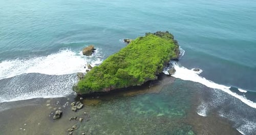 Aerial view of big coral rock on the shoreline with clear sea water and waves