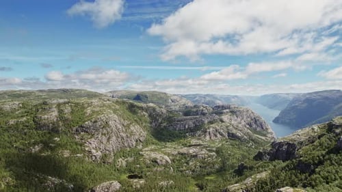 Aerial View Of Verdant Rugged Mountains And Scenic River Against Cloudy Blue Sky