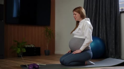 Pregnant Woman Kneels on Yoga Mat in Gym
