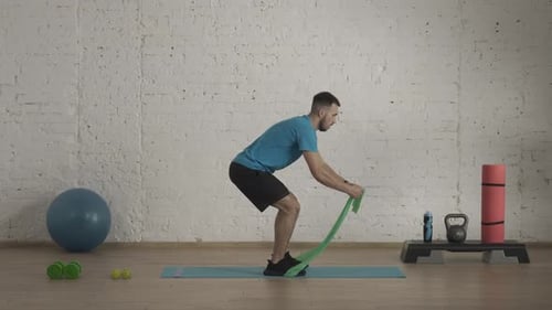 Man Fitness Coach in Sportswear Doing Half Squat Rubber Band Exercise for Online Class at the Home