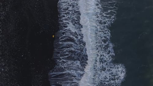 Top view of man running away for waves at black sand beach, aerial