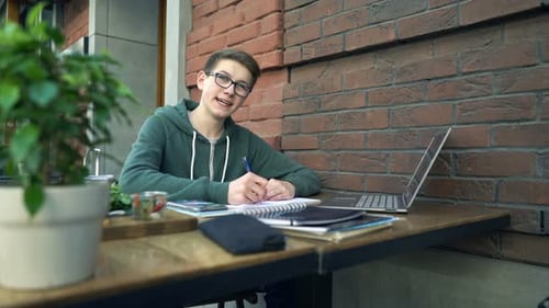 Happy Boy with Notepad Doing Homework by Table in Cafe Adolescent