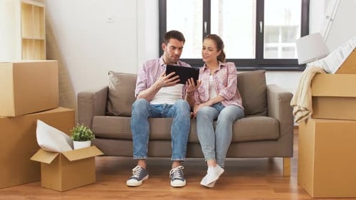 Couple with Tablet on Sofa Surrounded by Boxes