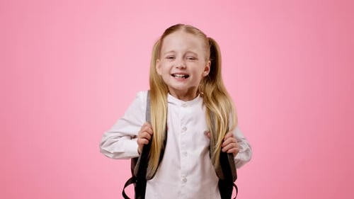 Mädchen mit langen Haaren lächelt, während sie Rucksack vor rosafarbenem Hintergrund trägt
