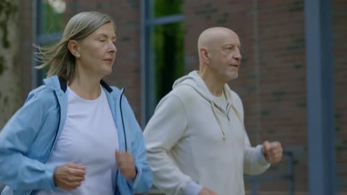 Side View of the Matured Sporty Couple Talking While Running in the Street