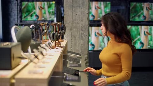 Une jolie jeune fille aux cheveux bouclés dans un pull orange choisit une montre intelligente dans un magasin