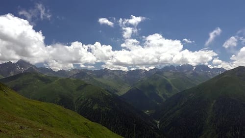 Chaîne montagneuse des Alpes avec ses vallées forestières verdoyantes et ses sommets escarpés sous des nuages estivaux spectaculaires.