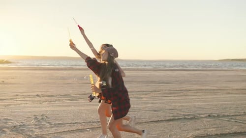 Two Girlfriends Wander Along the Beach During a Stunning Sunset Playfully Blowing Soap Bubbles That