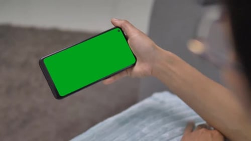 Close up view of woman hands using horizontal smartphone with key green screen. Chroma key mock up