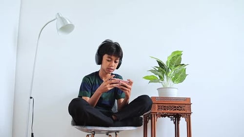 Teenager Gaming on Mobile Phone Indoors Wins