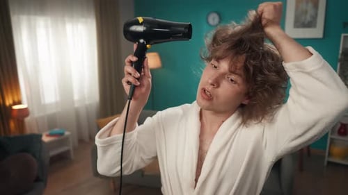 A Young Man with Curly Porous Hair Closeup Looking Into the Distance Holding a Hair Dryer He is