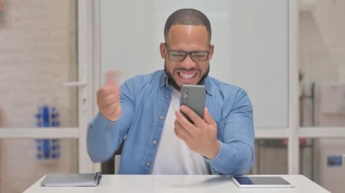 Excited Man Celebrating Smartphone Success at Work