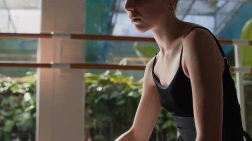 Elegante bailarina de ballet estirándose en el suelo en el estudio con la tranquila luz del sol