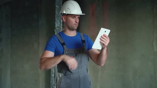 The Repairman Holds a Tablet in His Hands A Man in an Unfinished Building An Employee of a