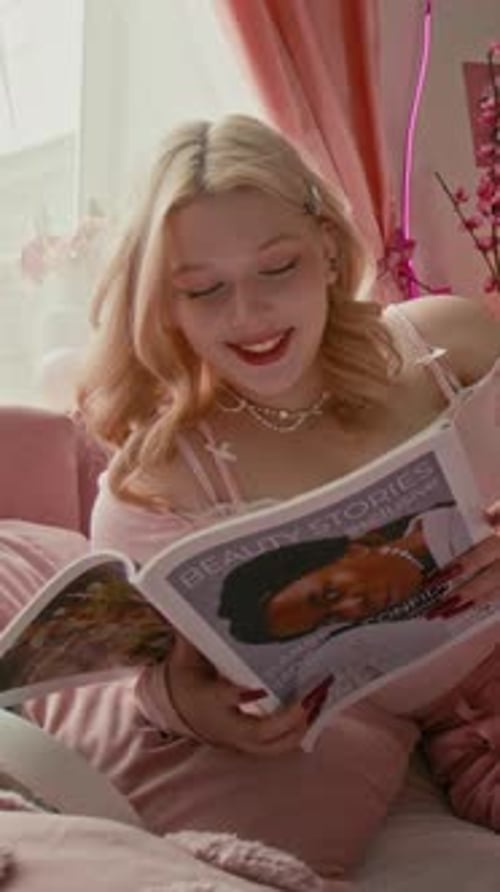 Blonde Girl Laughing While Flipping Through Beauty Magazine in Bed