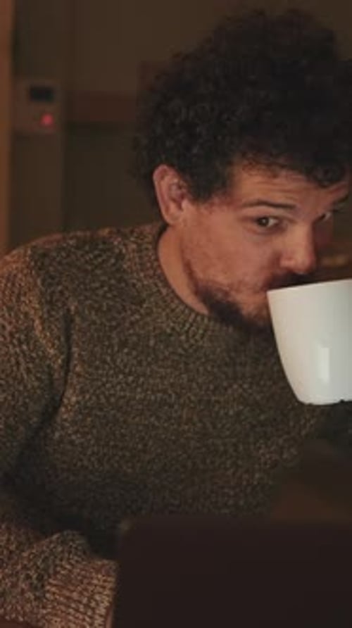 Young Adult Drinking Coffee Looking at Laptop At Night