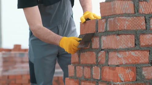 In yellow gloves. Close up view of construction man that is working with bricks.