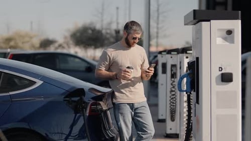 Mann überprüft das Telefon, während er das Elektroauto an der Station auflädt