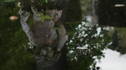 Tilt up across classical stone statue and reflection in slow motion calming fountain water