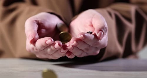 Coins falling into woman's hands at wooden table, closeup