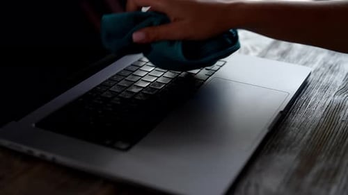 Woman Cleans Laptop with Spray and Cloth Indoors