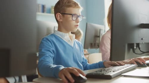 Elementary School Classroom: Portrait of a Smart Boy with Glasses Uses Personal Computer, Learning