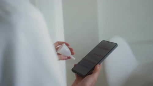 Unknown Girl Holding Menstrual Cup and Phone with Period Calendar on Screen