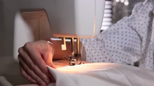 Woman sewing fabric with professional machine in workshop, closeup