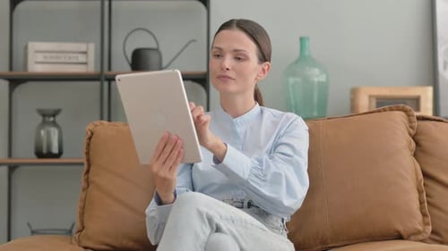 Young Woman Using Tablet on Brown Couch Indoors