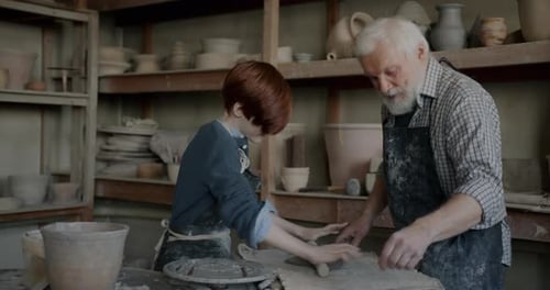 Happy Child Making Artwork From Clay Learning Pottery From Grandpa in Traditional Studio