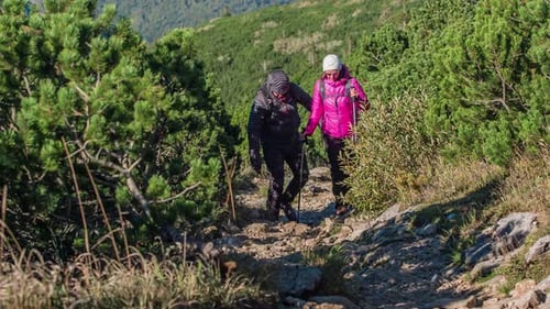 Hiker couple trekking through the rocky and uneven mountainous terrain on a bright sunny morning. Sl