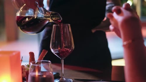waiter is filling guest's glass with red wine in a restaurant. 4K. dim light romantic dinner