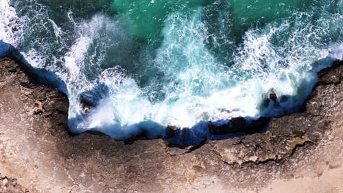 Foamy ocean waves hitting rocky shore with power, aerial top down view