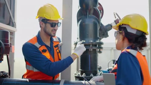 Two industrial engineers discussing maintenance while inspecting pipes and valves at a manufacturing
