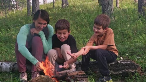 Family Roasting Sausages Around Campfire in Woods