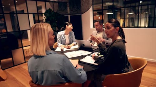Two Young Businesswomen Talking Together While Working with Colleagues Around an Office