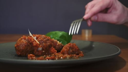 Side View of a Man taking a Fork and start eating Meatballs in Tomato Sauce, well presented dish and