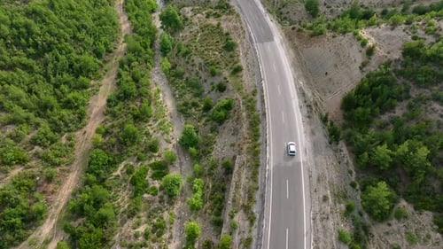 Aerial View of Cars Driving on a Highway Winding Through Green Hilly Terrain with Rocky Outcrops