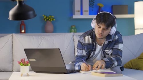 Männlicher Student, der Musik hört und nachts studiert.