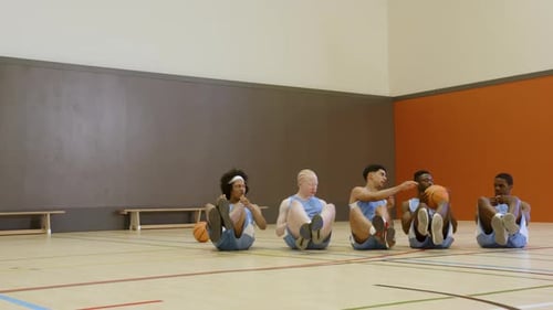 Basketball team doing core exercises in gym, focused on fitness training