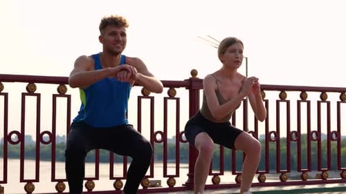 Smiling Couple Warming Up While Crouching Before Jogging Standing on the Bridge River on the