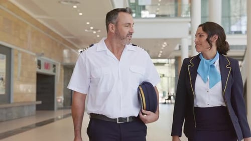 Smiling Pilot and Stewardess Walking Together and Discussing at Airport. Experienced Commercial