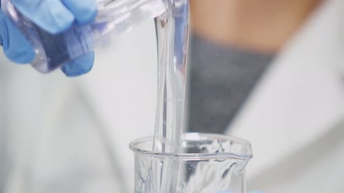 L'assistant verse du mucus clair dans un verre de laboratoire vide