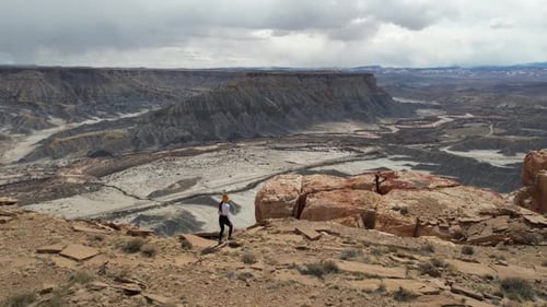 Drone Shot of Woman Walking Alone on Top of Mesa Above Deep Canyon, Abyss and Desert Landscape
