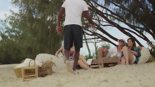 A Handsome Black Man Walks Up To Picnic Area To Sit With His Friends On The Beach In Australia Wi...