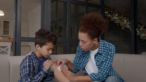 Portrait of Caring African American Mom Treating Injured Son's Knee with Bandage