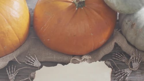 Paper with copy space against skeleton hands and pumpkins on wooden surface