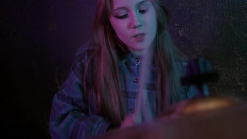 Cute Young Woman Playing Drums in the Studio with Blue and Pink Lighting